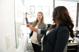 Two professionals writing on a whiteboard with markers