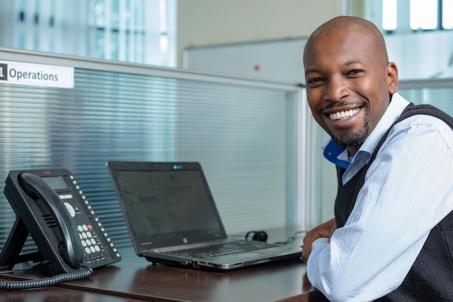 Professional at a desk with a laptop and desk phone smiling for the camera