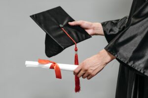 Hand extending diploma and graduation cap.