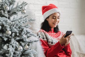 Woman in Santa hat looking at phone and smiling.