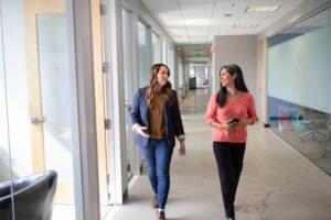 Two professionals walking down an office hallway and talking.