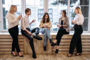 Five coworkers talking near an office window.