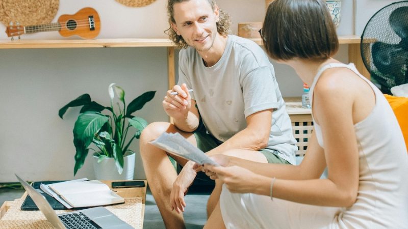A man and a woman conversing over a table. There's a notebook and a laptop in front of them.