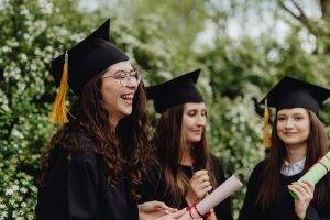 Three graduates outside, in caps and gowns, smiling.