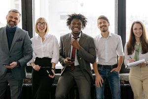 Group of smiling coworkers standing in front of an office window.