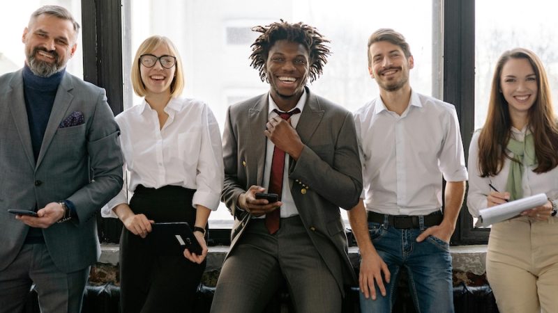 Group of smiling coworkers standing in front of an office window.