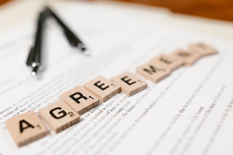 An employment agreement on a table top with two pens and tiles spelling out the word agreement.
