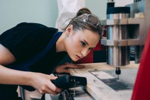 Woman with safety glasses on top of her head looking at work machinery.
